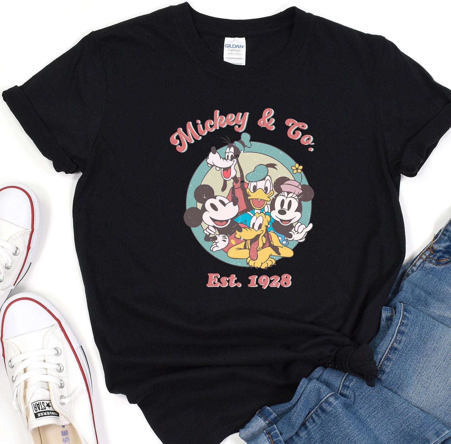 a mickey mouse and friends t - shirt sitting on top of a pair of jeans