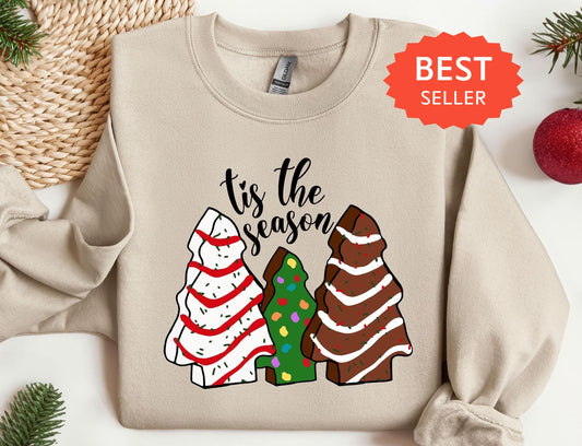 a sweater that says tis the season next to a christmas tree