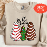 a sweater that says tis the season next to a christmas tree