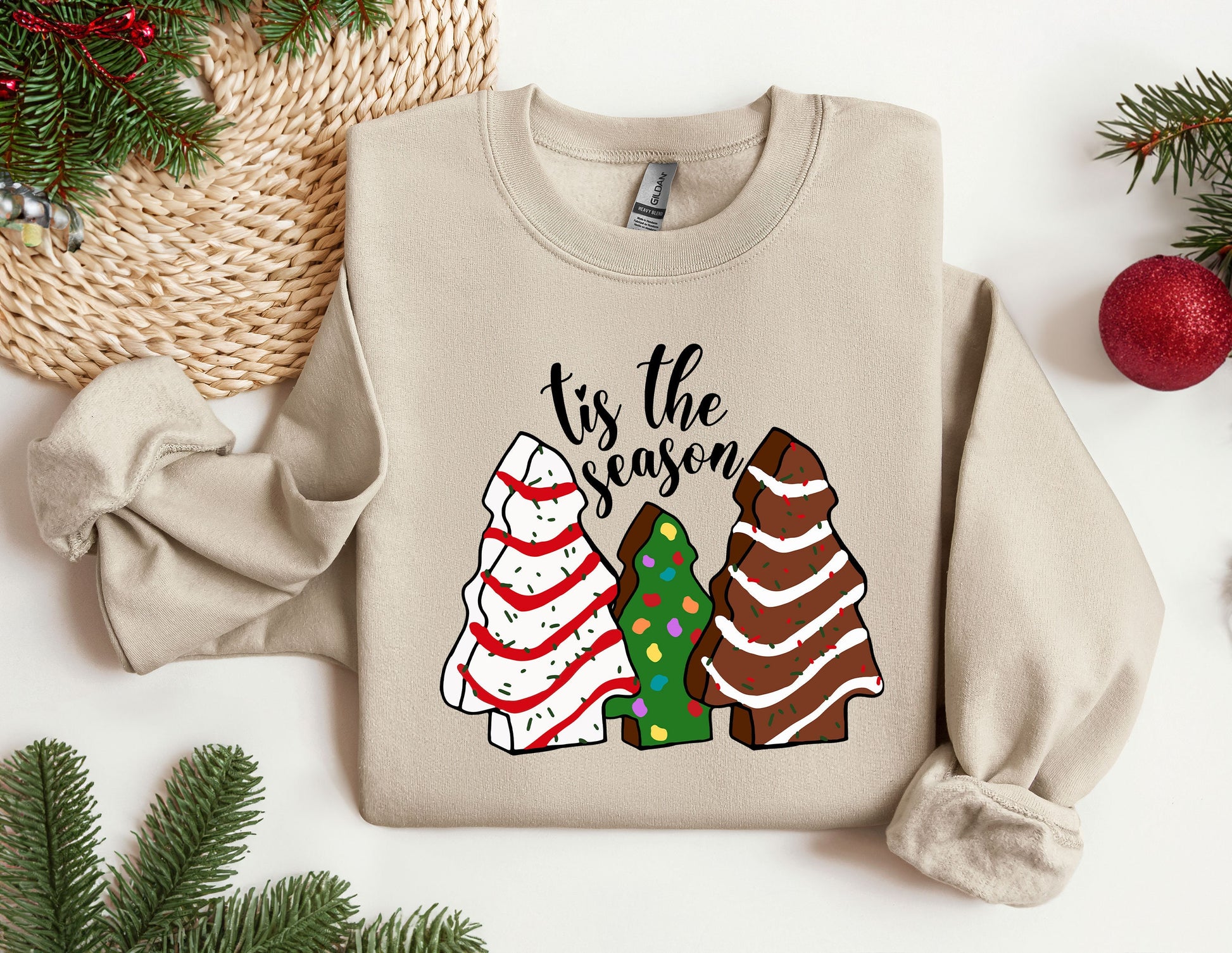 a sweater that says tis the season next to a christmas tree