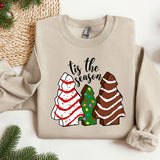 a sweater that says tis the season next to a christmas tree