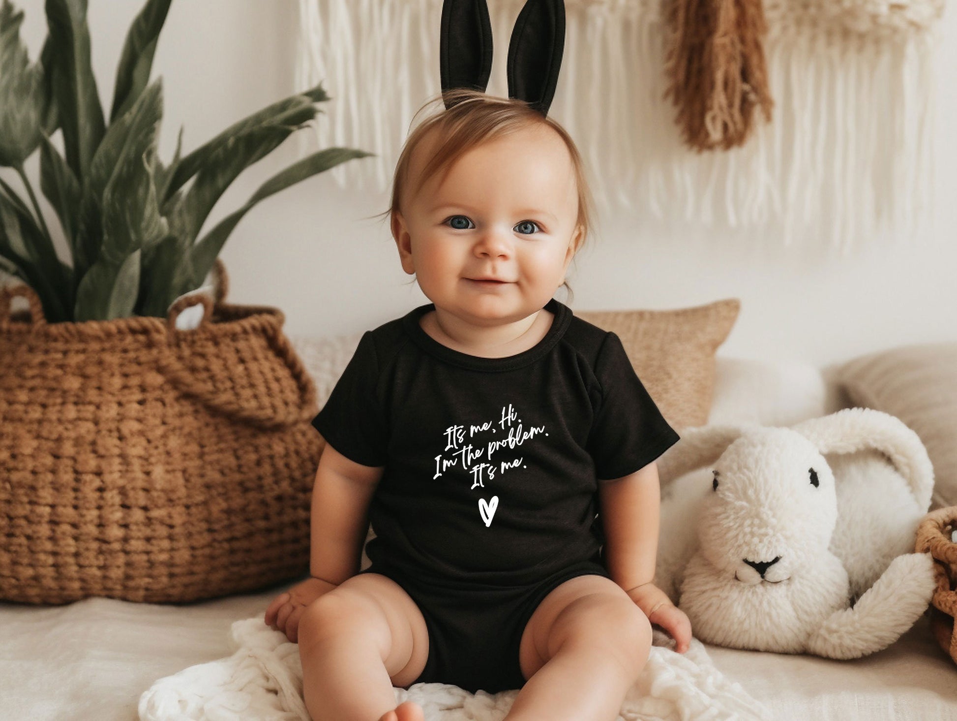 a baby sitting on a bed wearing a black shirt with a bunny ears on it