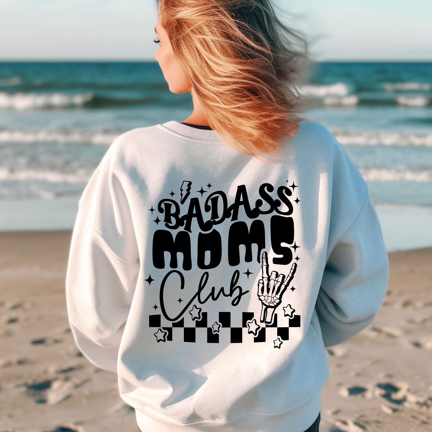 a woman standing on a beach wearing a sweatshirt