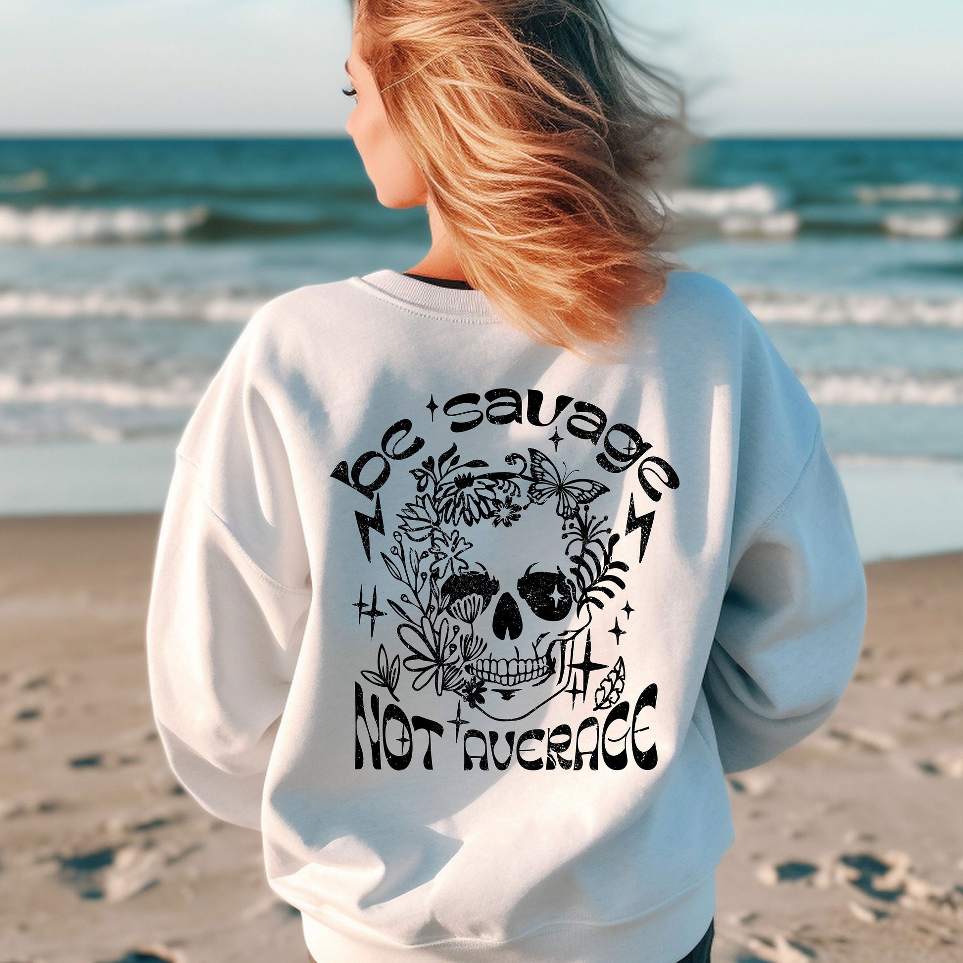 a woman standing on a beach wearing a white sweatshirt