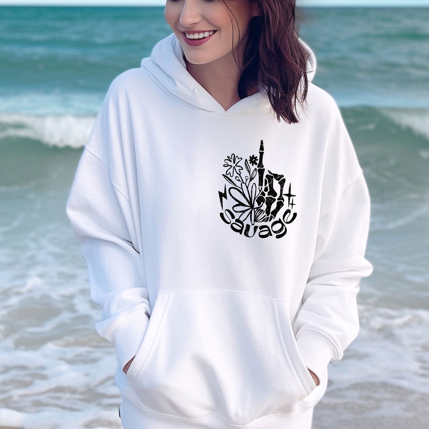 a woman standing on the beach wearing a white hoodie