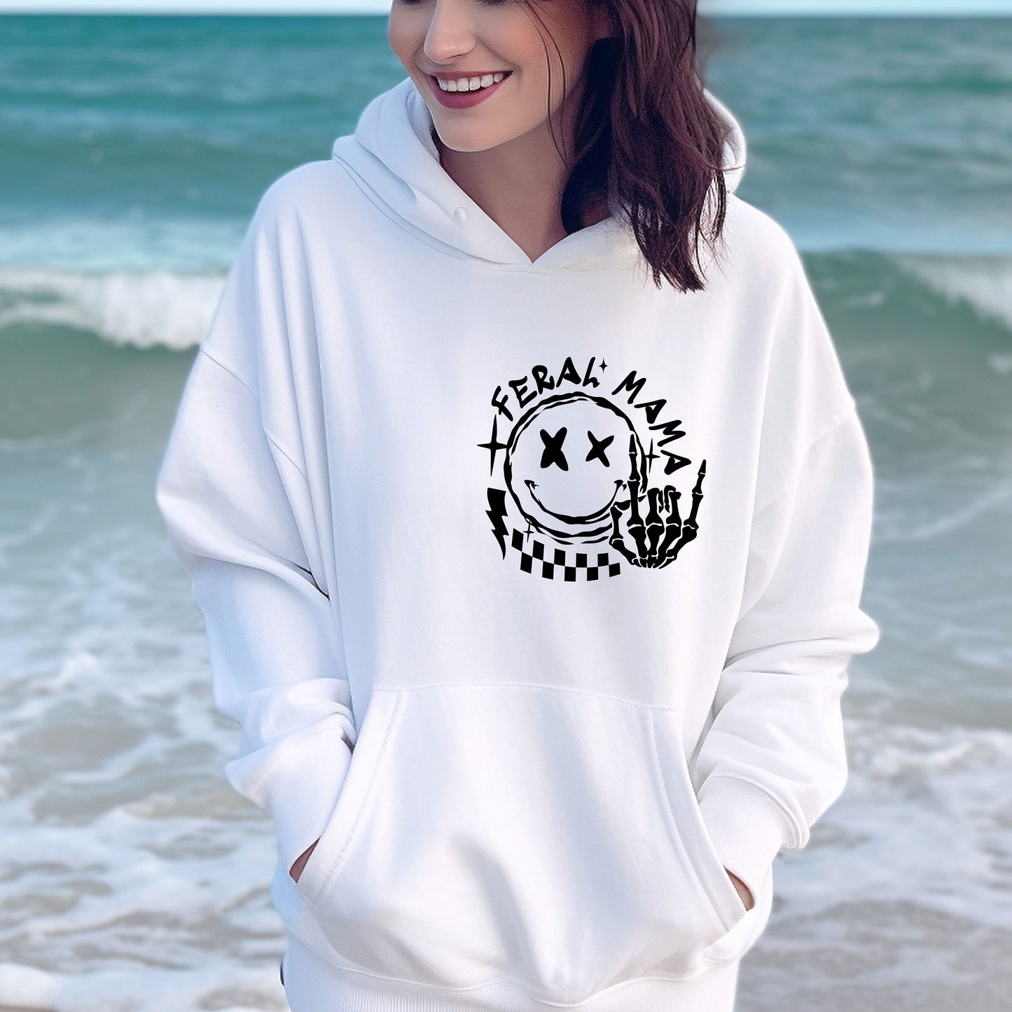 a woman standing on the beach wearing a white hoodie