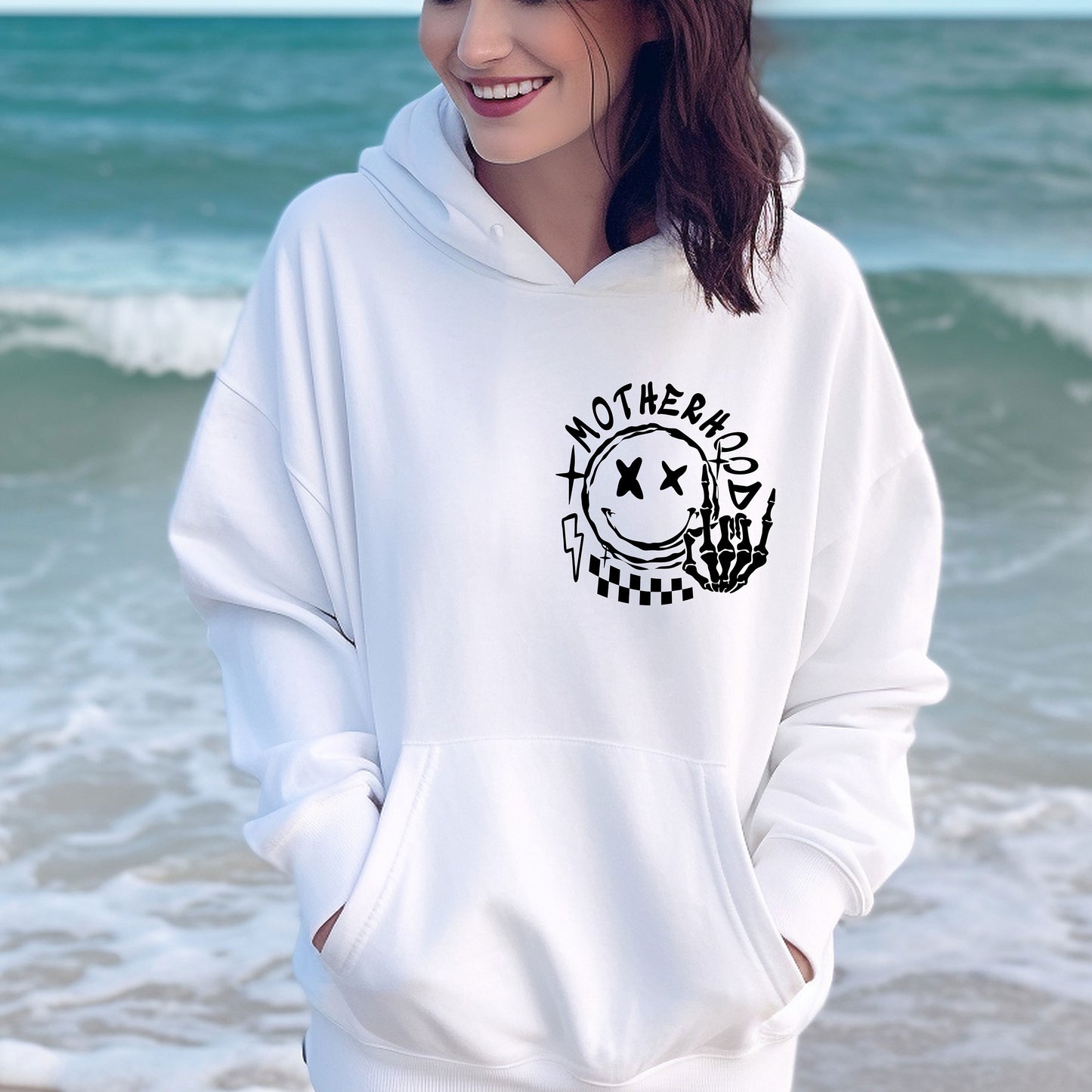 a woman standing on the beach wearing a white hoodie