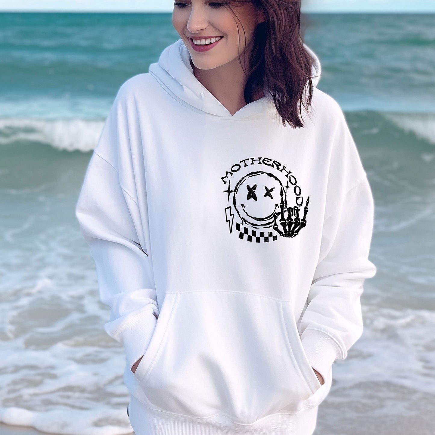 a woman standing on the beach wearing a white hoodie