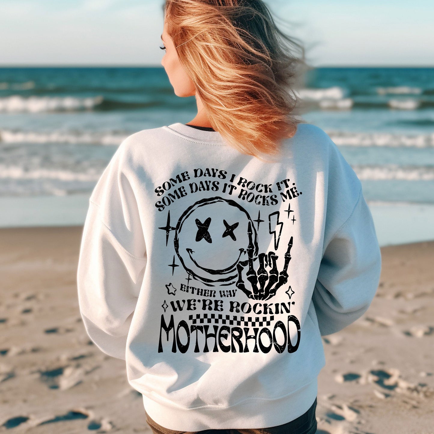 a woman standing on a beach wearing a sweatshirt