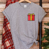 a t - shirt with a gift box on it next to a christmas tree