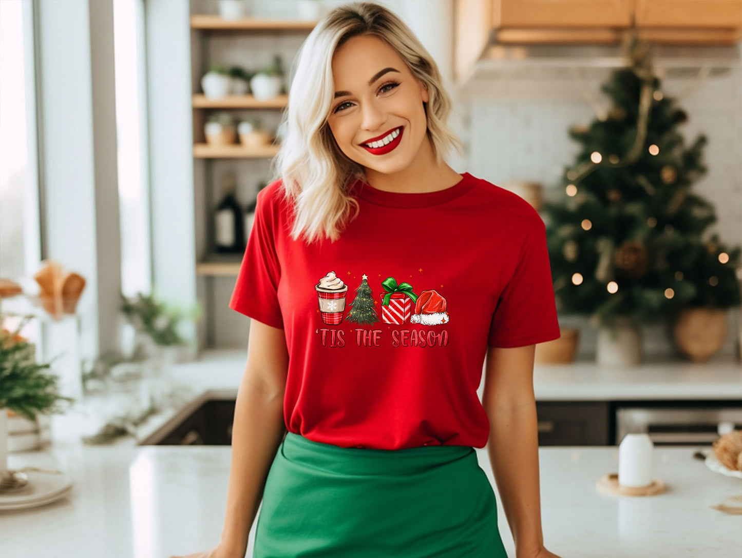 a woman standing in a kitchen wearing a red shirt and green skirt