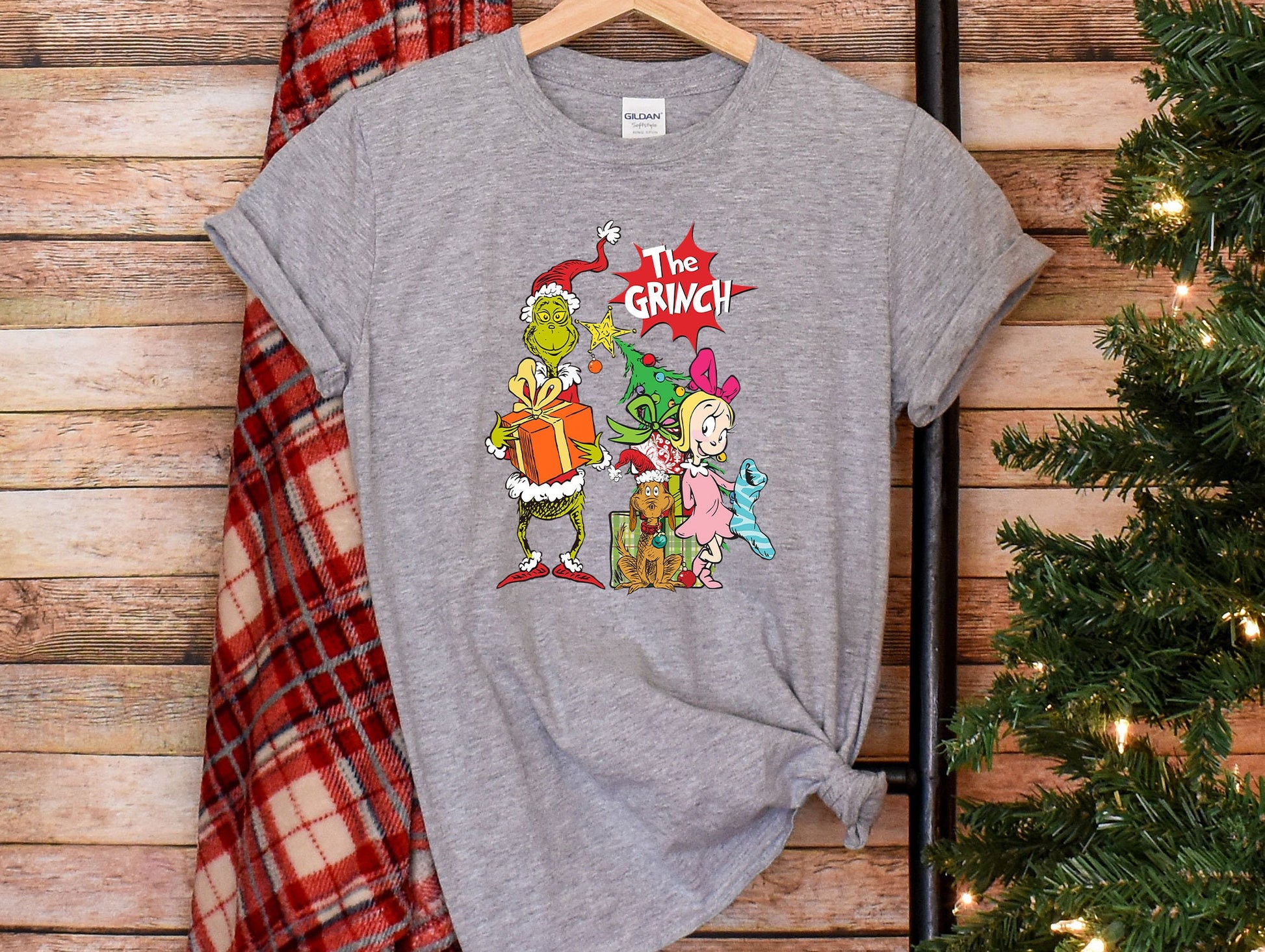 a gray t - shirt with the grinch on it next to a christmas tree