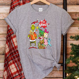 a gray t - shirt with the grinch on it next to a christmas tree