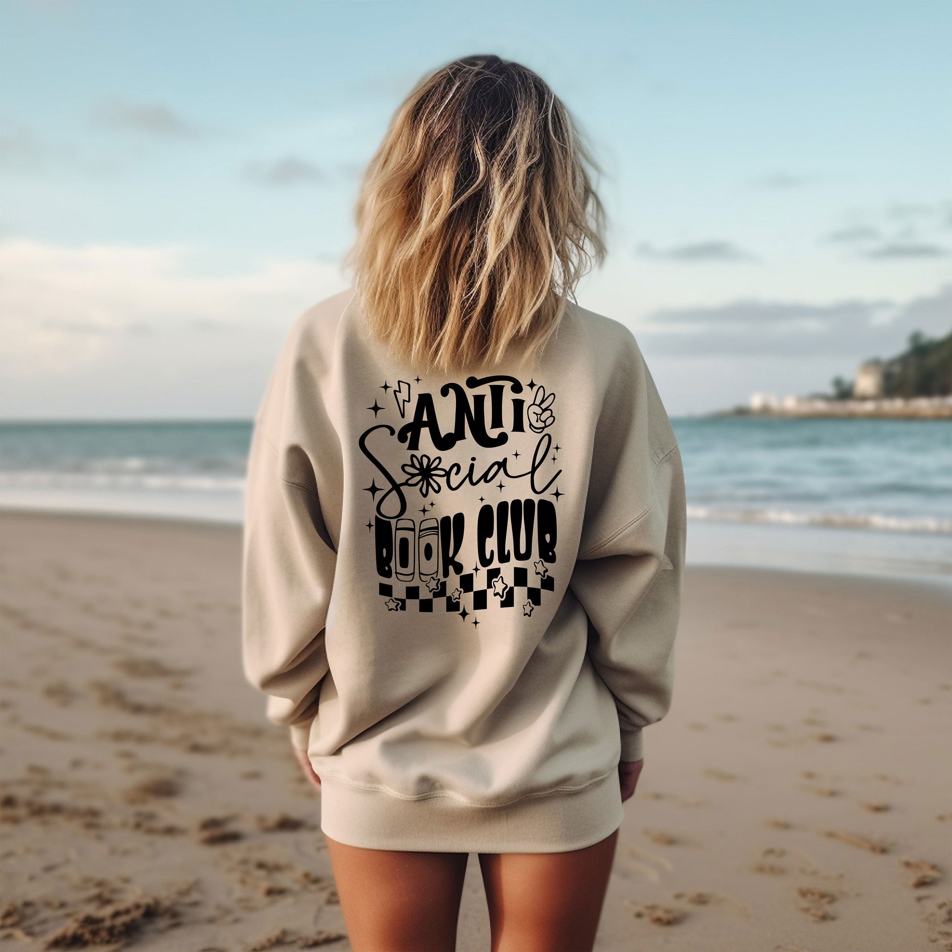 a woman standing on a beach wearing a sweatshirt