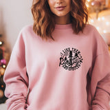 a woman standing in front of a christmas tree wearing a pink sweatshirt
