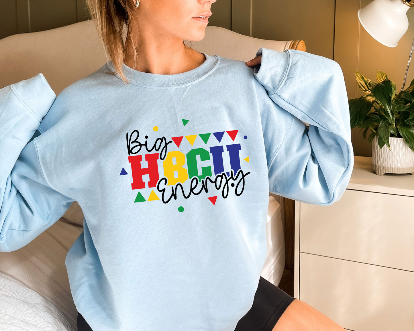 a woman sitting on a bed wearing a blue sweatshirt