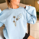 a woman sitting on a bed wearing a blue sweater with flowers on it