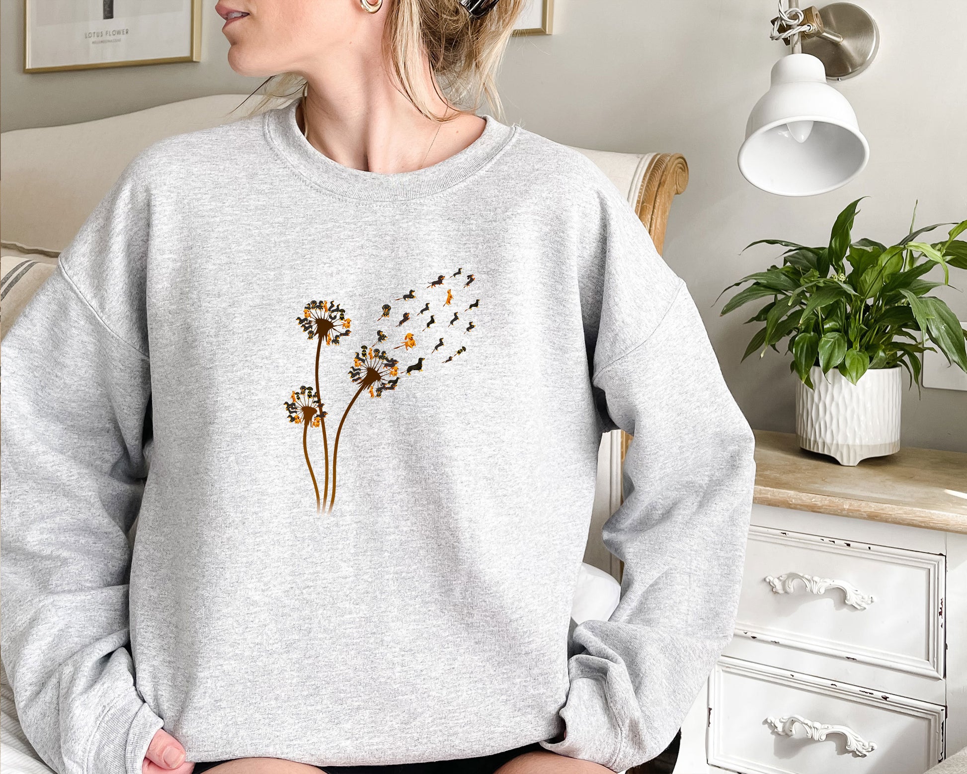 a woman sitting on a bed wearing a sweatshirt with a dandelion on it