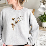 a woman sitting on a bed wearing a sweatshirt with a dandelion on it