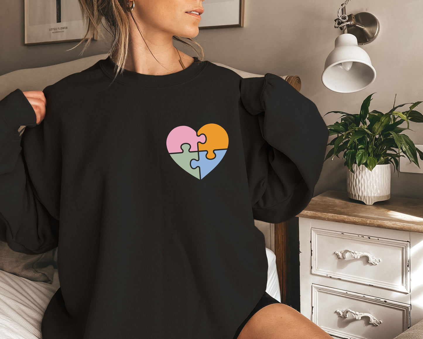 a woman sitting on a bed wearing a black sweatshirt with a puzzle heart on it