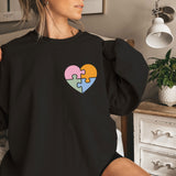 a woman sitting on a bed wearing a black sweatshirt with a puzzle heart on it