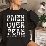a woman sitting on a bed wearing a black sweatshirt that says faith over fear