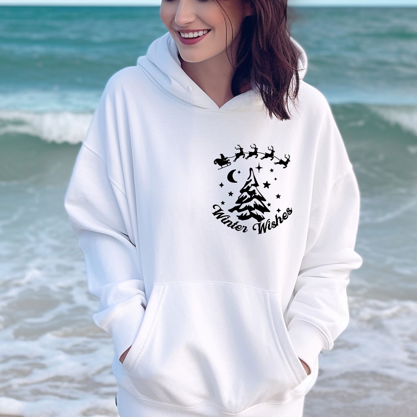 a woman standing on the beach wearing a white hoodie