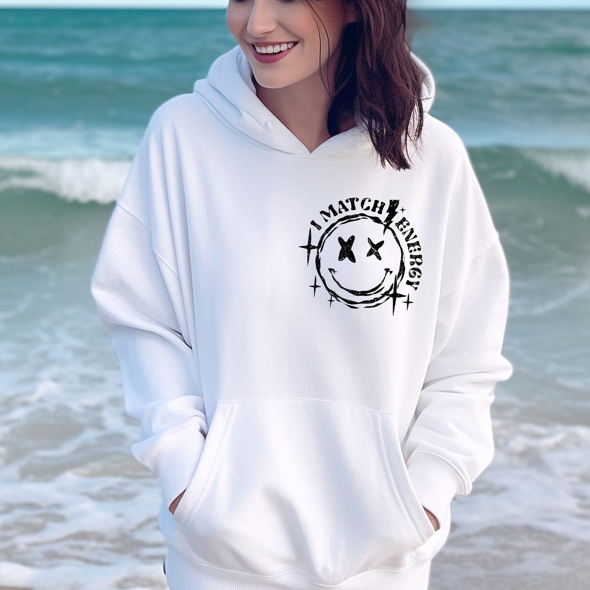 a woman standing on the beach wearing a white hoodie