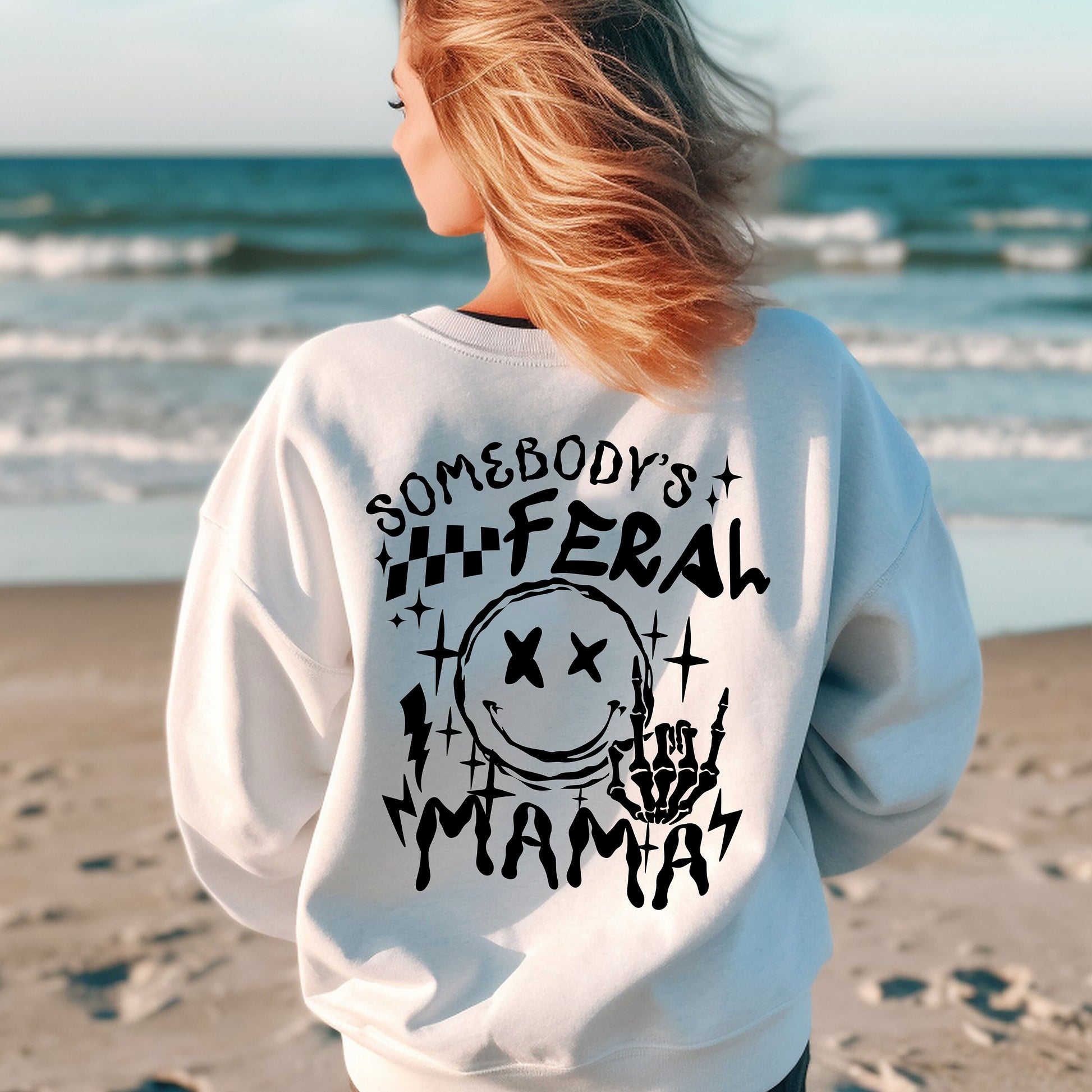 a woman standing on a beach wearing a sweatshirt