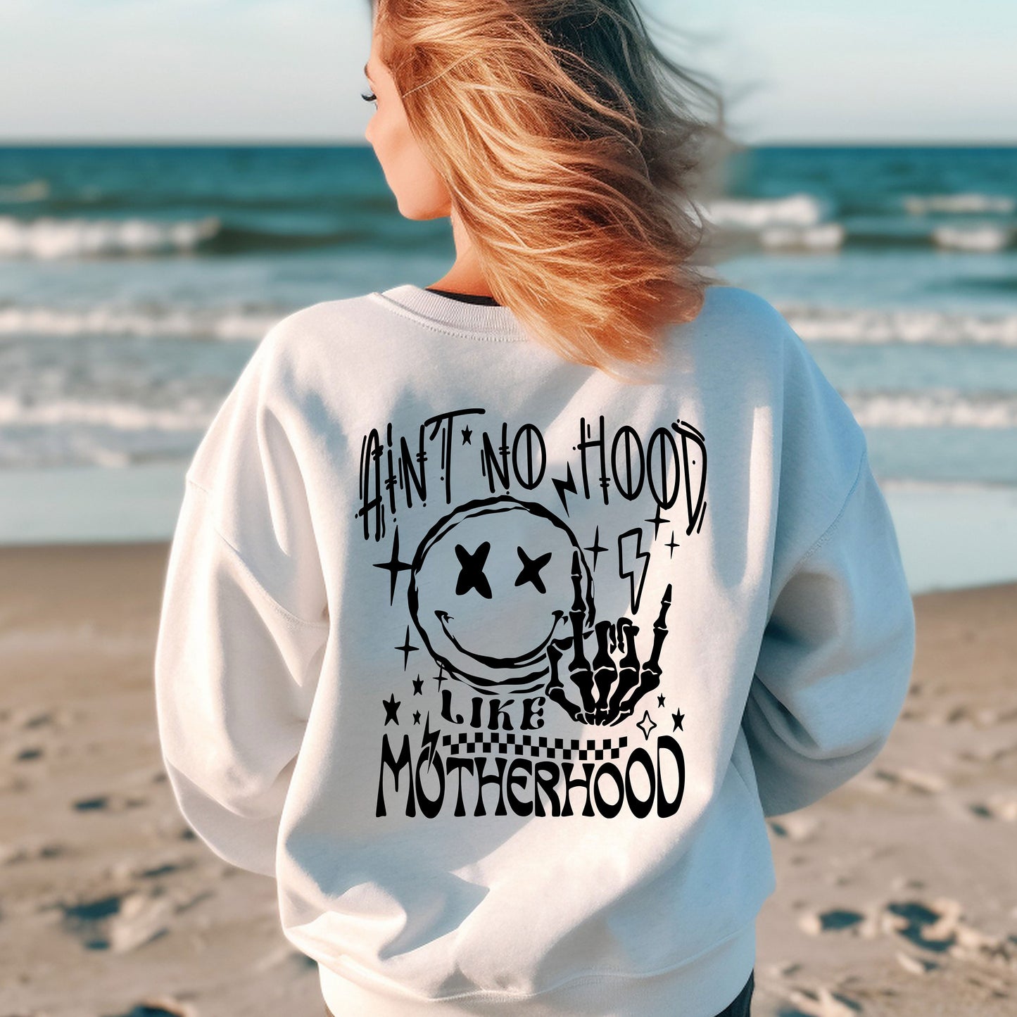 a woman standing on a beach wearing a sweatshirt