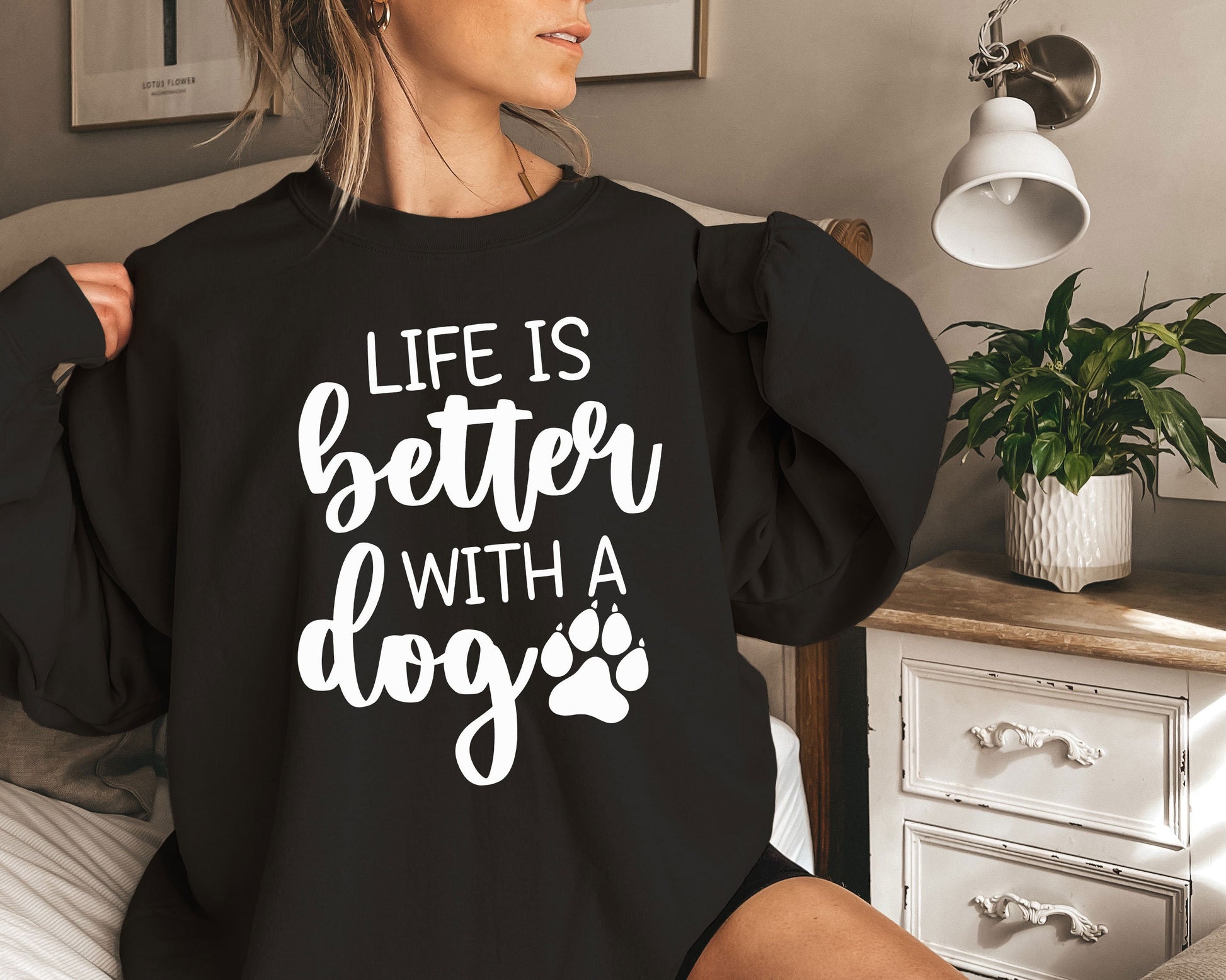 a woman sitting on a bed wearing a black sweatshirt that says life is better with