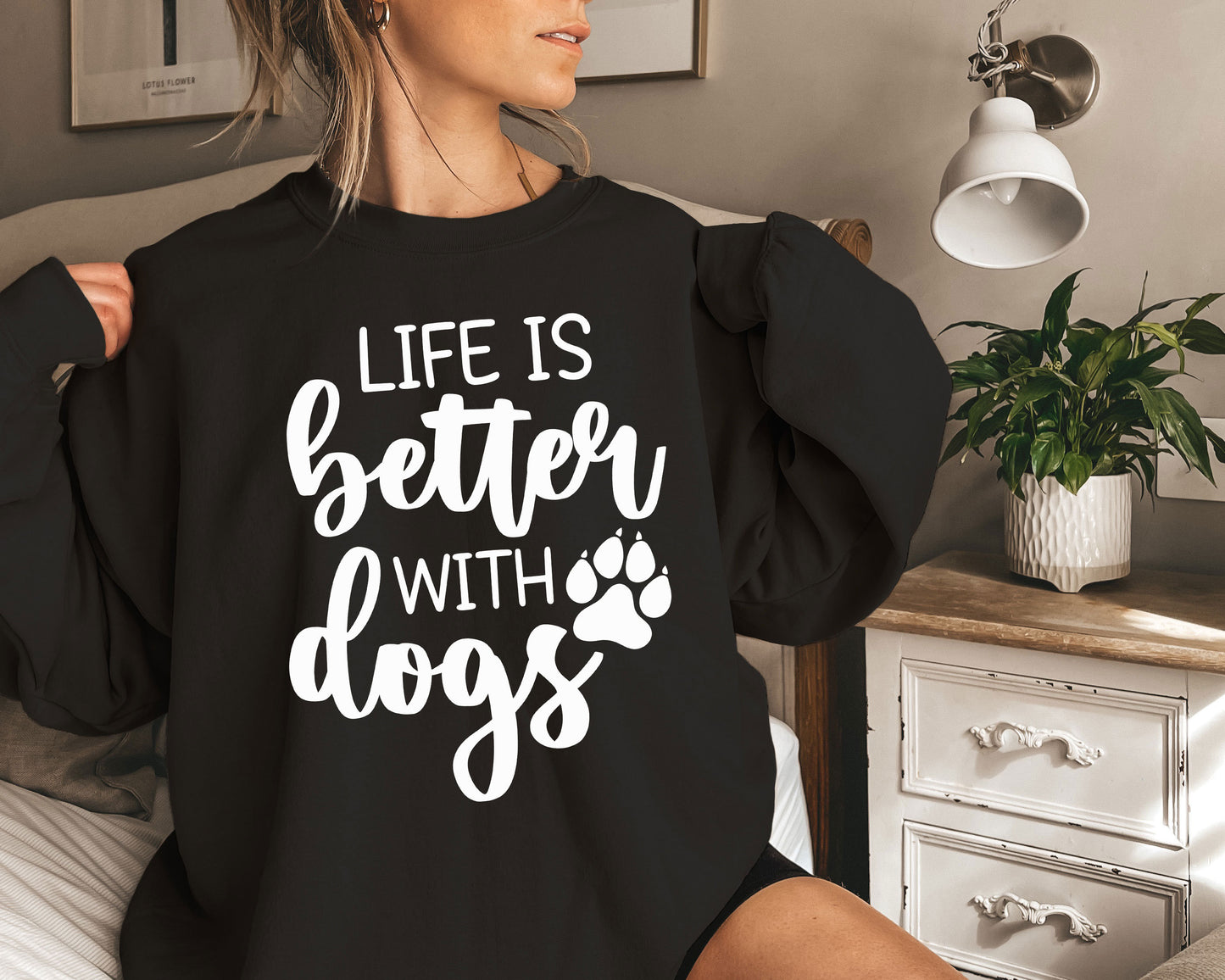 a woman sitting on a bed wearing a black sweatshirt that says life is better with