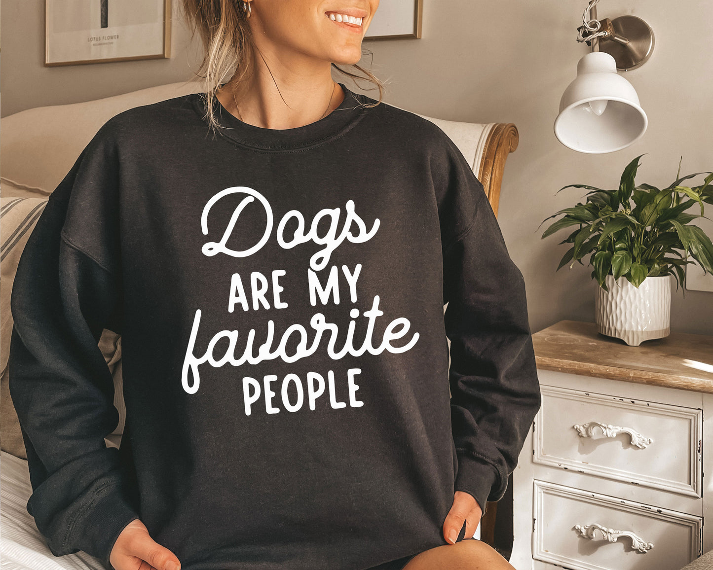 a woman sitting on a bed wearing a sweatshirt that says dogs are my favorite people