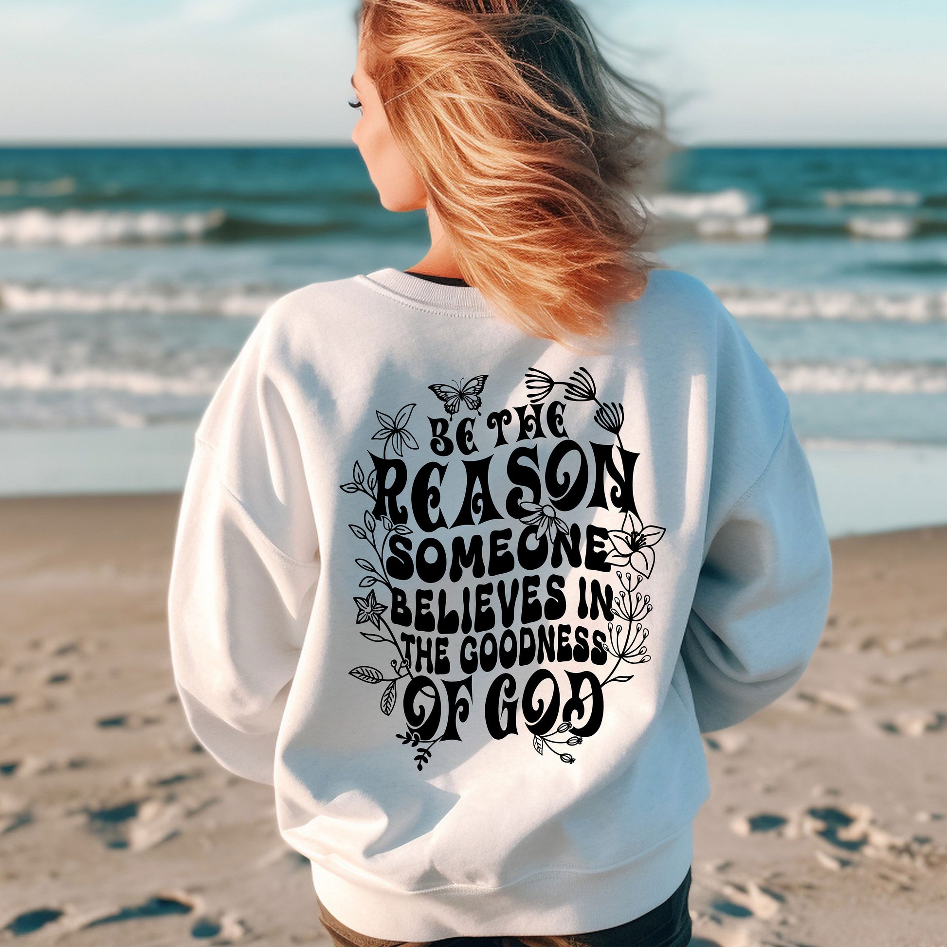 a woman standing on a beach wearing a sweatshirt