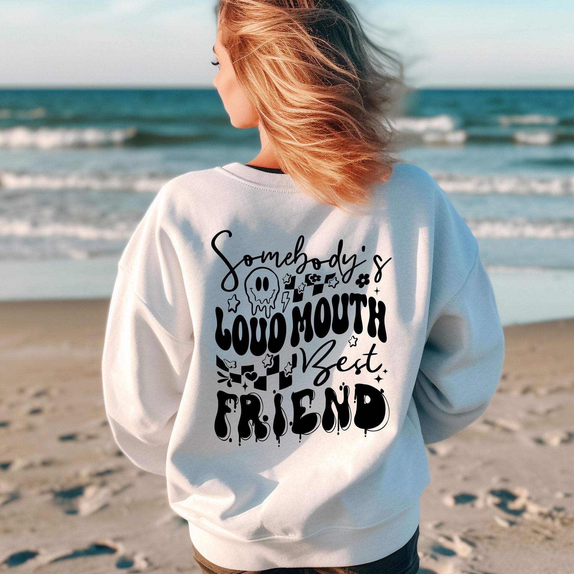 a woman standing on a beach wearing a sweatshirt