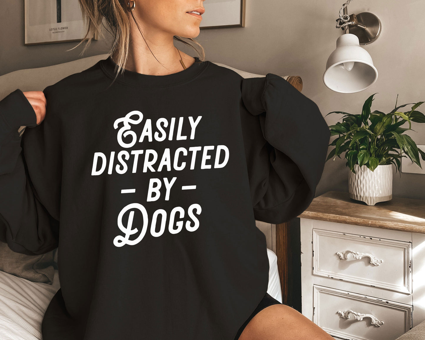 a woman sitting on a bed wearing a black sweatshirt that says easily distracted by dogs