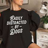 a woman sitting on a bed wearing a black sweatshirt that says easily distracted by dogs