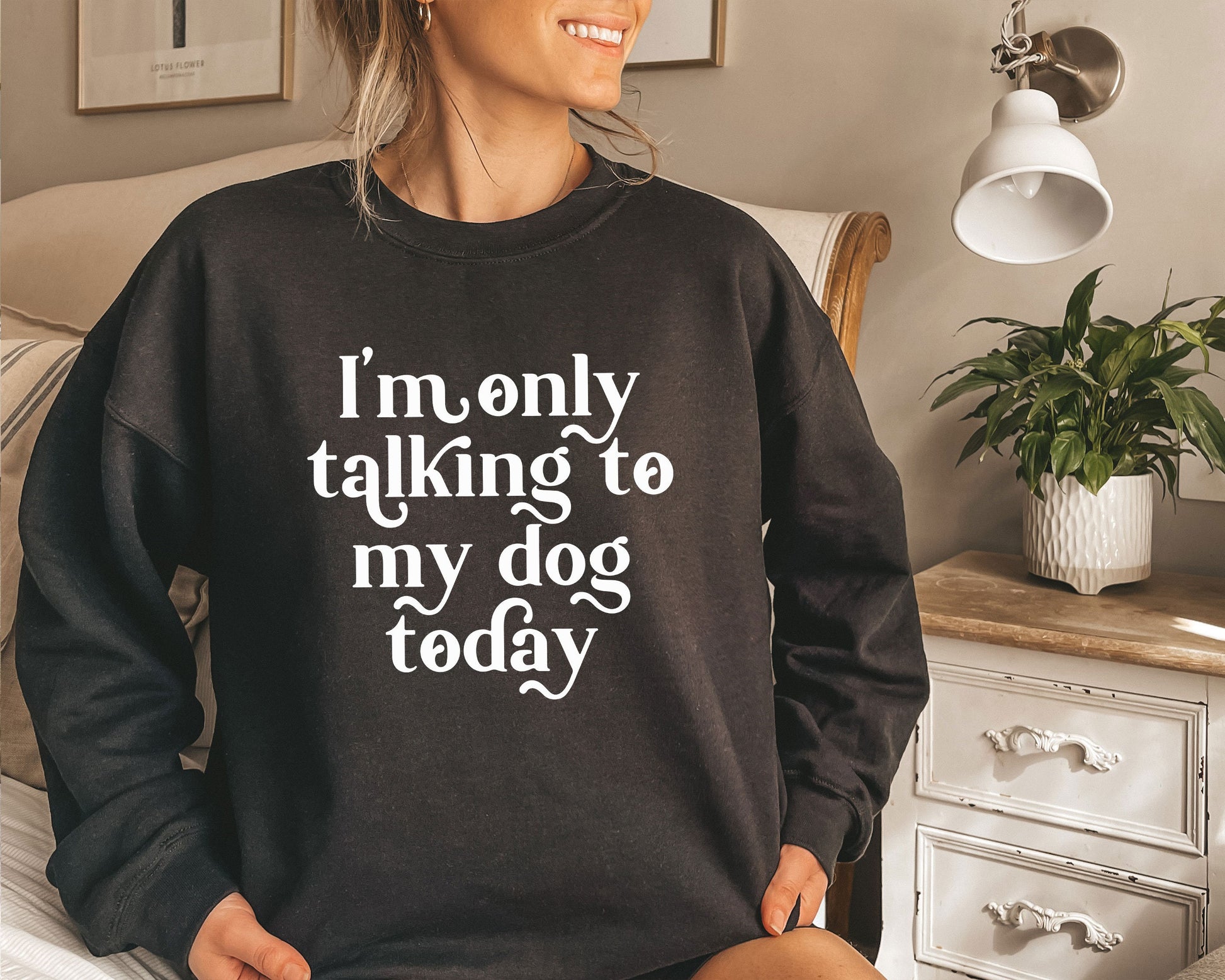 a woman sitting on a bed wearing a black sweatshirt that says i&#39;m only