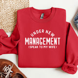 a red sweater that says under new management speak to my wife