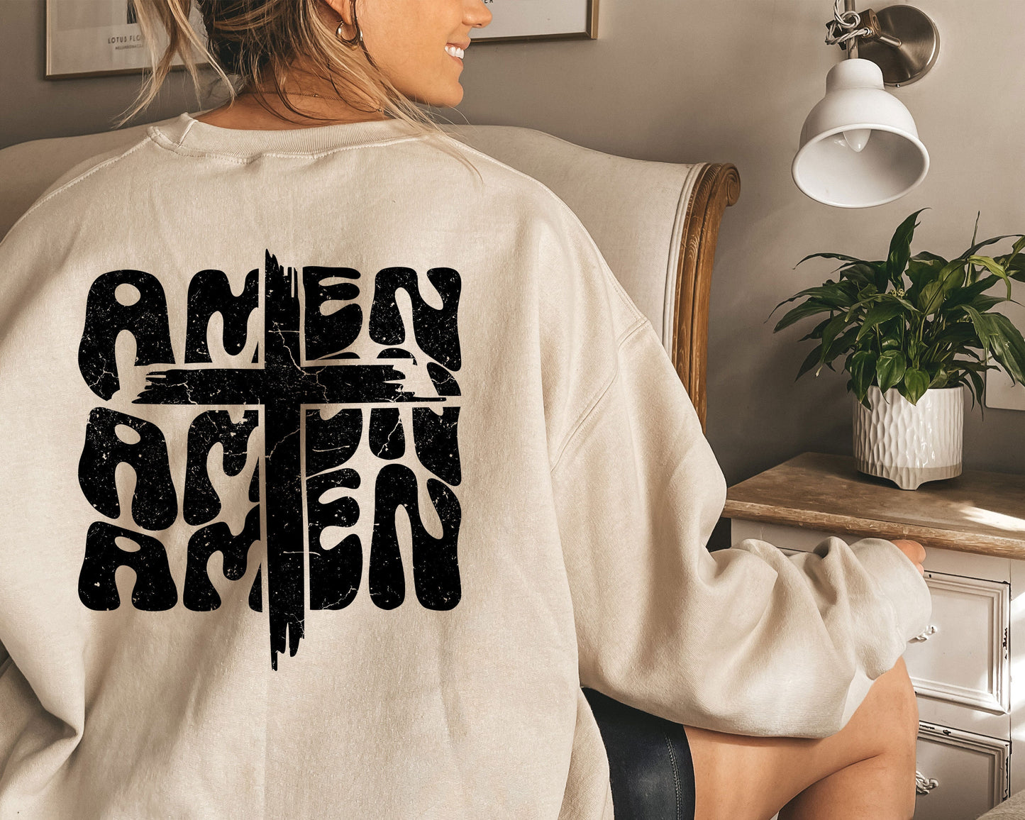 a woman sitting in a chair wearing a sweatshirt with a cross on it