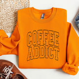 an orange sweatshirt that says coffee addict next to a pair of sneakers