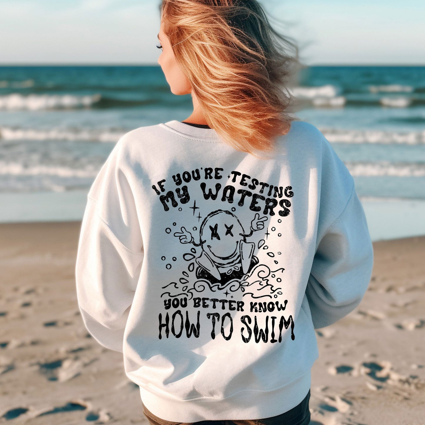 a woman standing on a beach wearing a sweatshirt