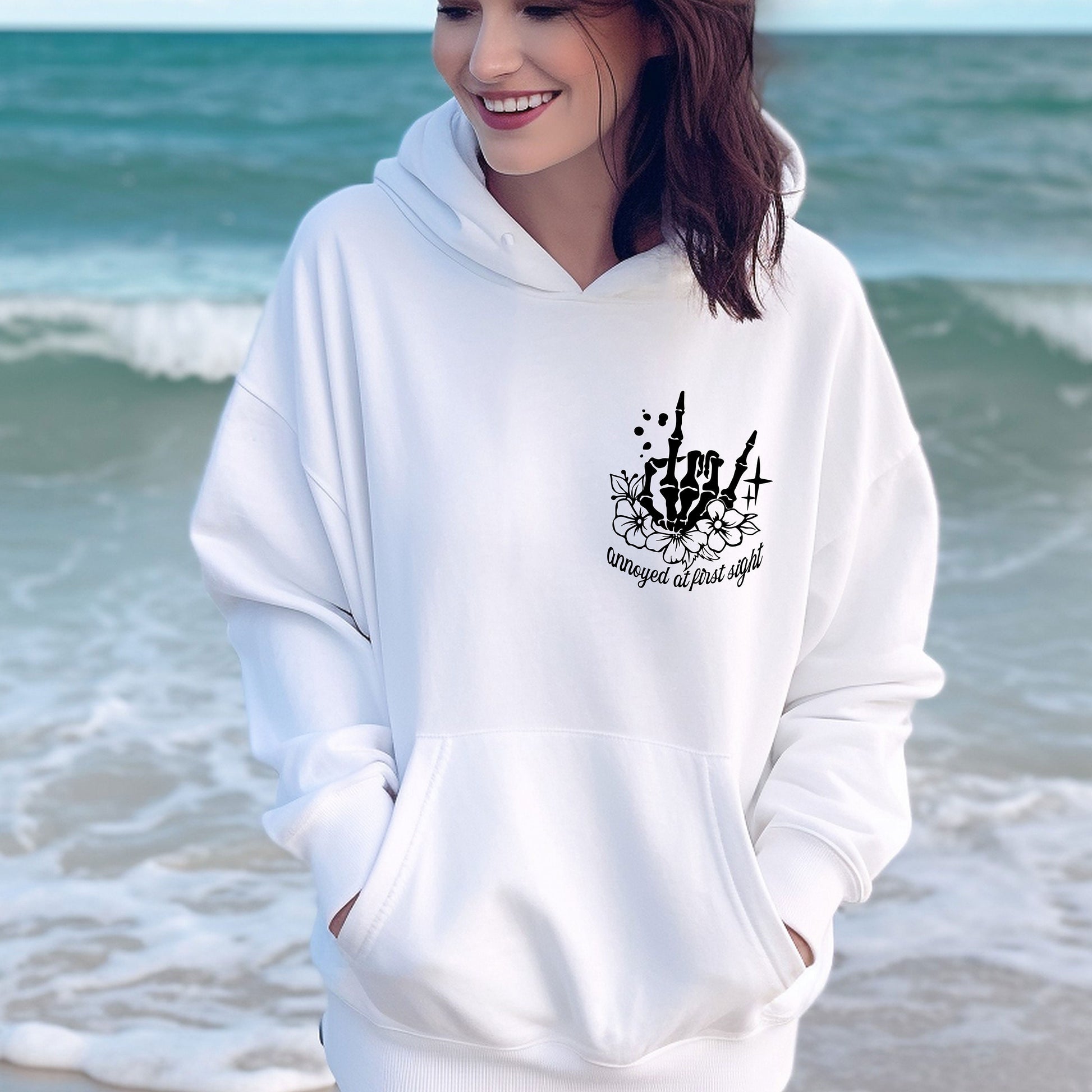 a woman standing on the beach wearing a white hoodie