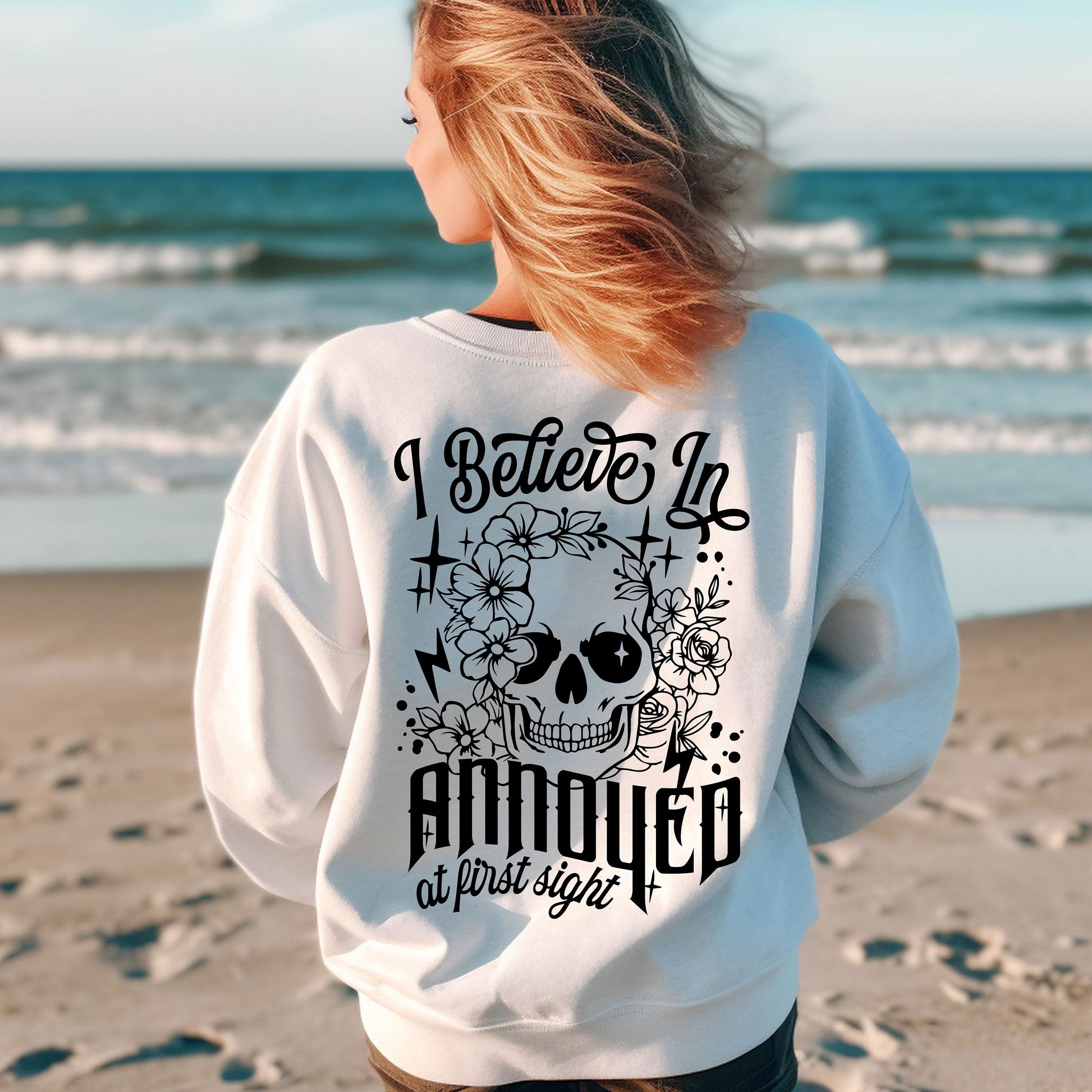 a woman standing on a beach wearing a sweatshirt