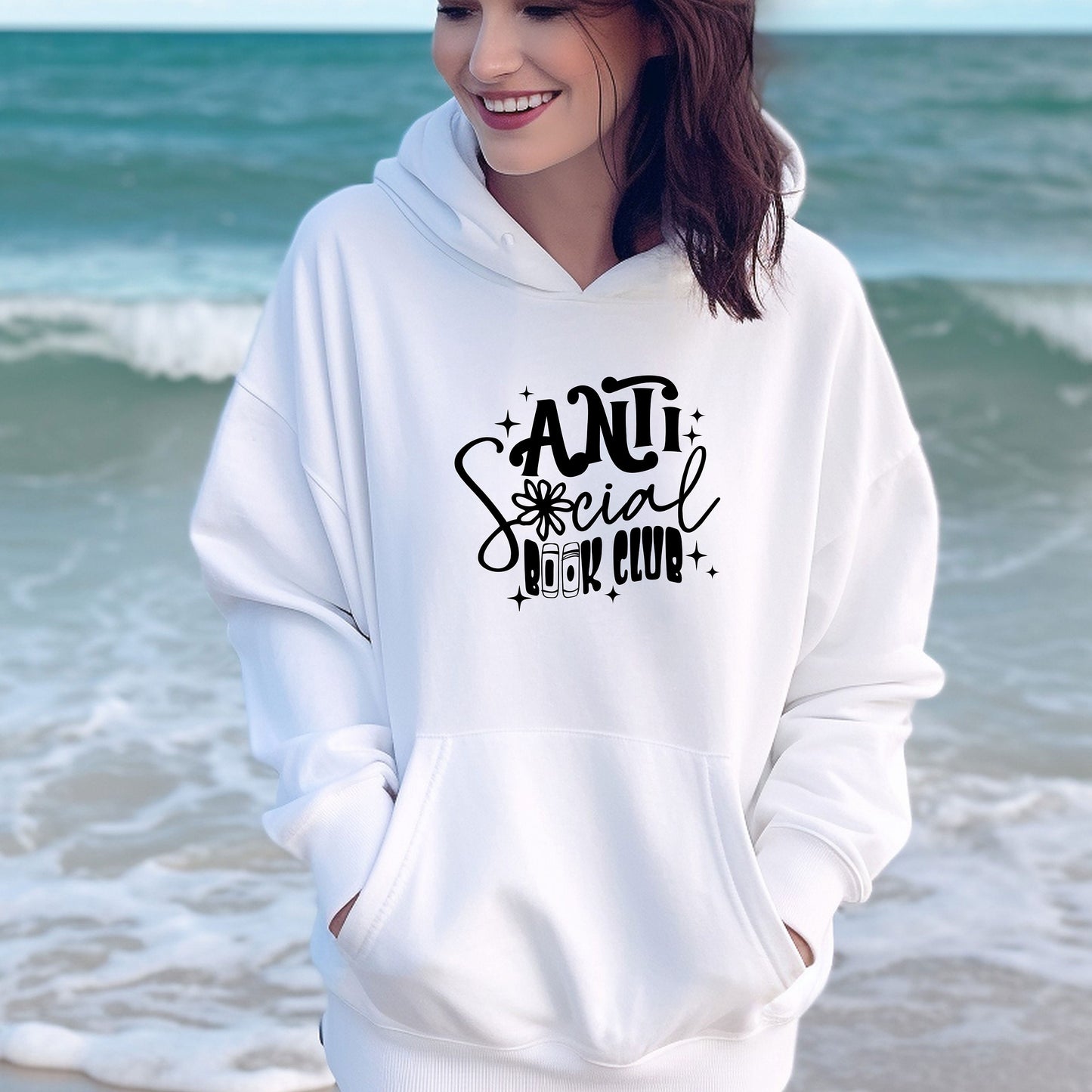 a woman standing on the beach wearing a white hoodie