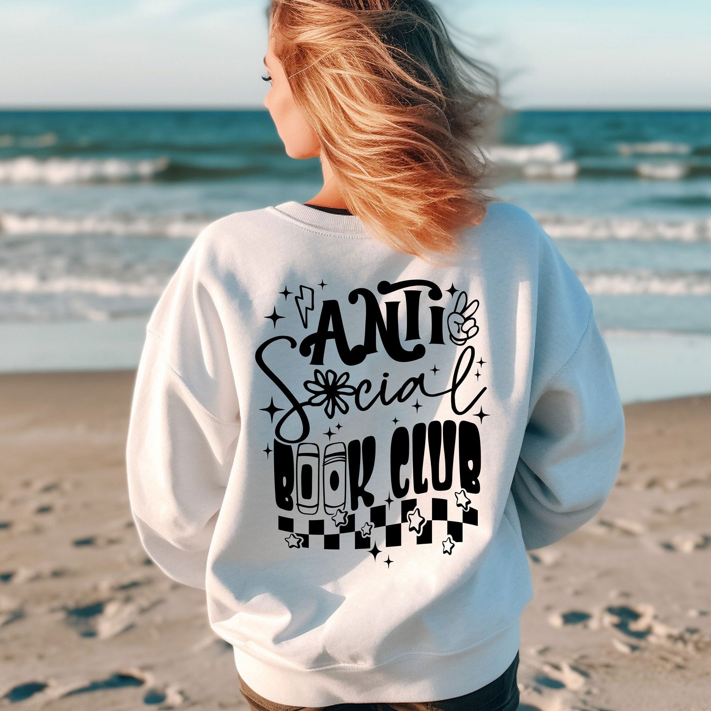 a woman standing on a beach wearing a sweatshirt