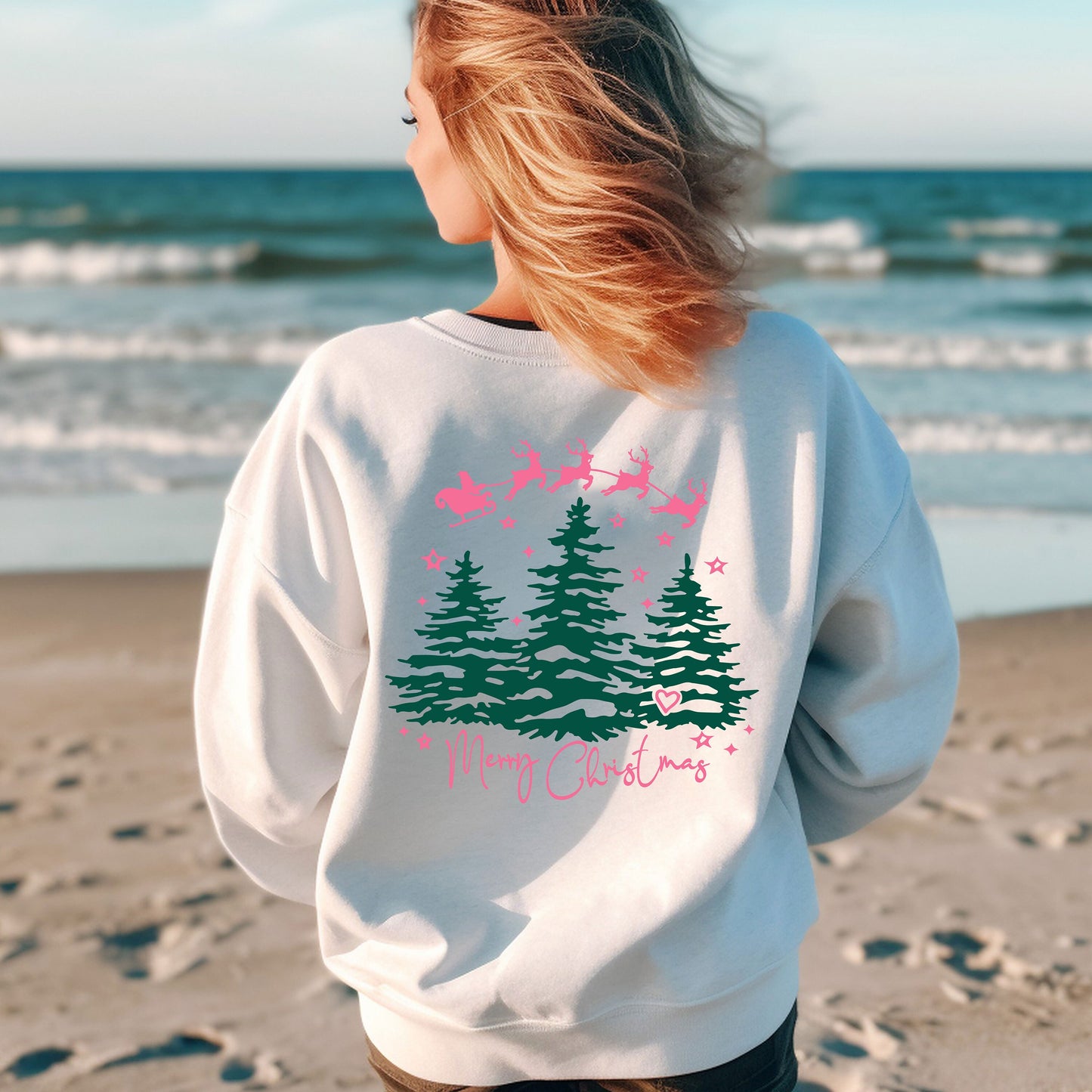 a woman standing on a beach wearing a sweatshirt with trees on it