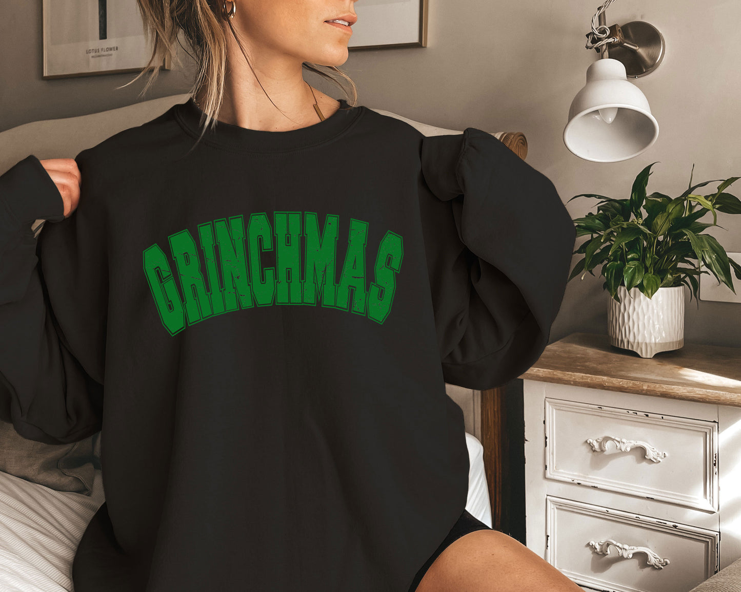 a woman sitting on a bed wearing a black sweatshirt with green lettering