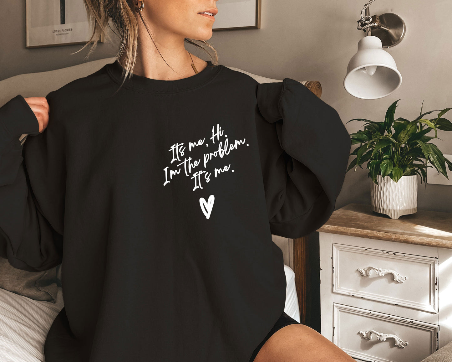 a woman sitting on a bed wearing a black sweatshirt