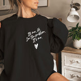a woman sitting on a bed wearing a black sweatshirt